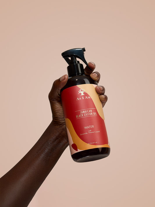 As I Am Jamaican Black Castor Oil Water - Porträtaufnahme der feuchtigkeitsspendenden Sprühflasche in der Hand, die die leichte, mit JBCO angereicherte Formel zur Erfrischung und Befeuchtung natürlicher Locken hervorhebt.