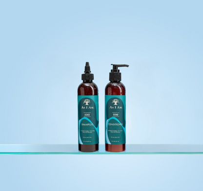 Zwei Flaschen As I Am Shampoo und Conditioner auf einer klaren Oberfläche mit hellblauem Hintergrund