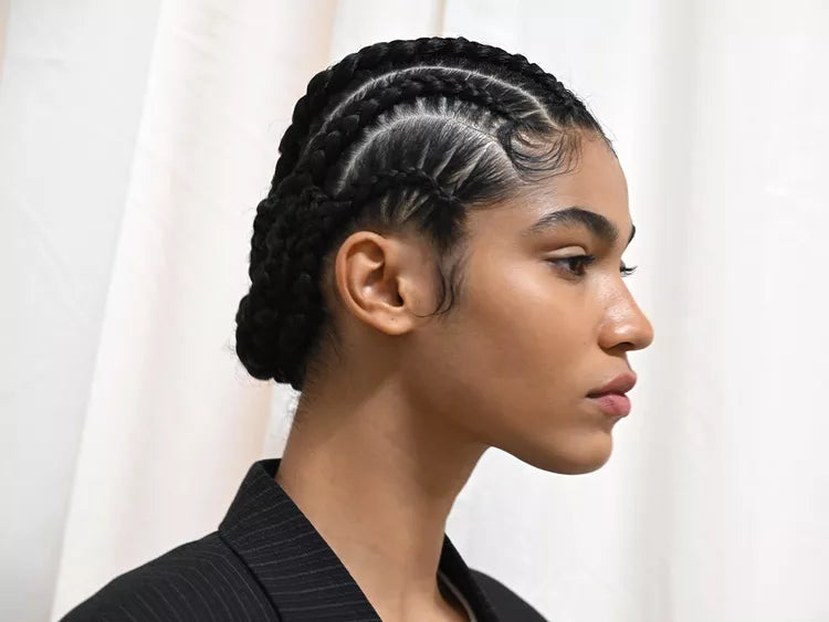 Frau mit geflochtenen Haaren, die ein schwarzes Outfit trägt, vor einem weißen Vorhanghintergrund