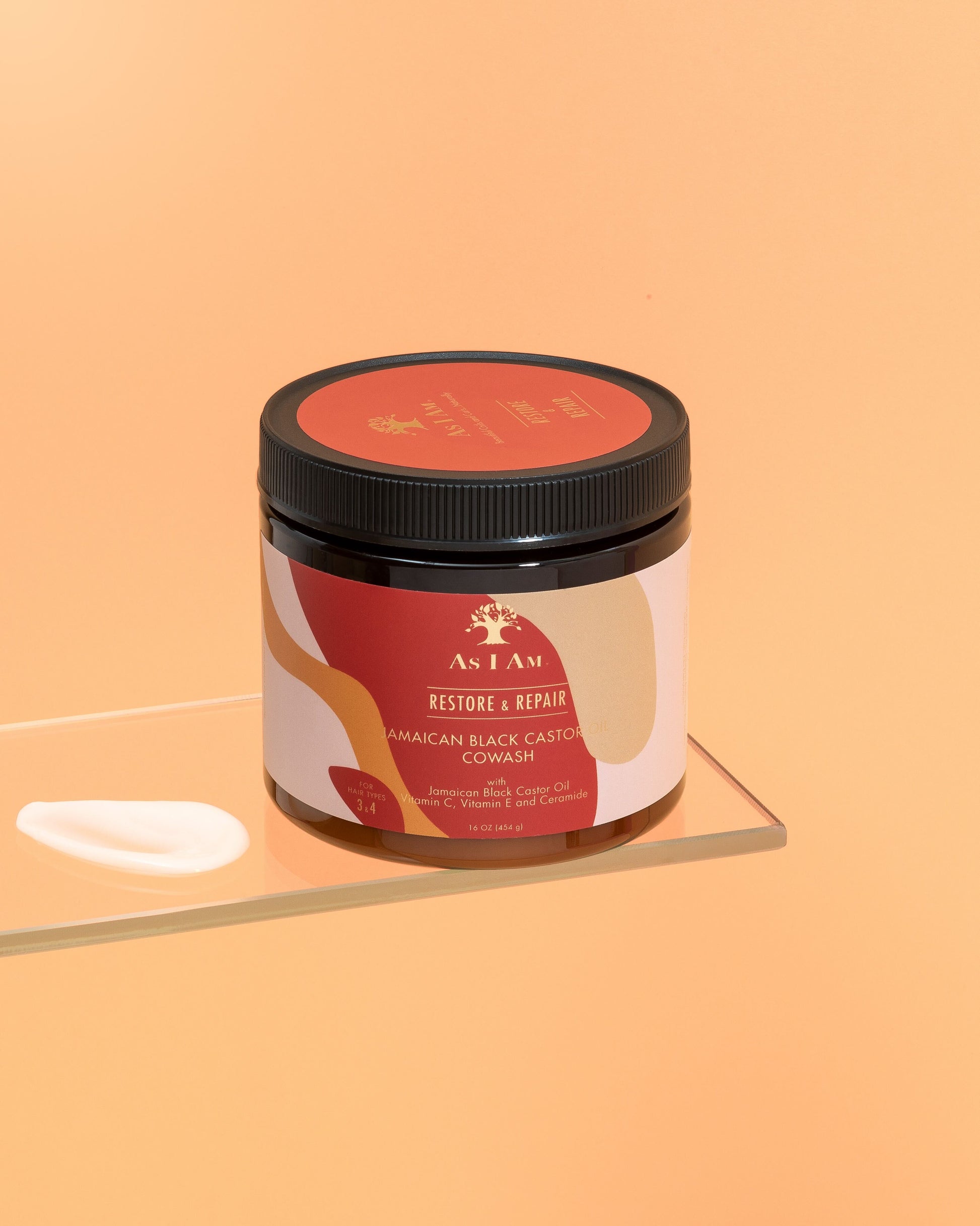 Ein Behälter mit jamaikanischem Black Castor Oil Cowash mit einem Etikett, auf dem die Produktdetails angegeben sind, auf einer reflektierenden Oberfläche mit einem einfarbigen orangefarbenen Hintergrund.