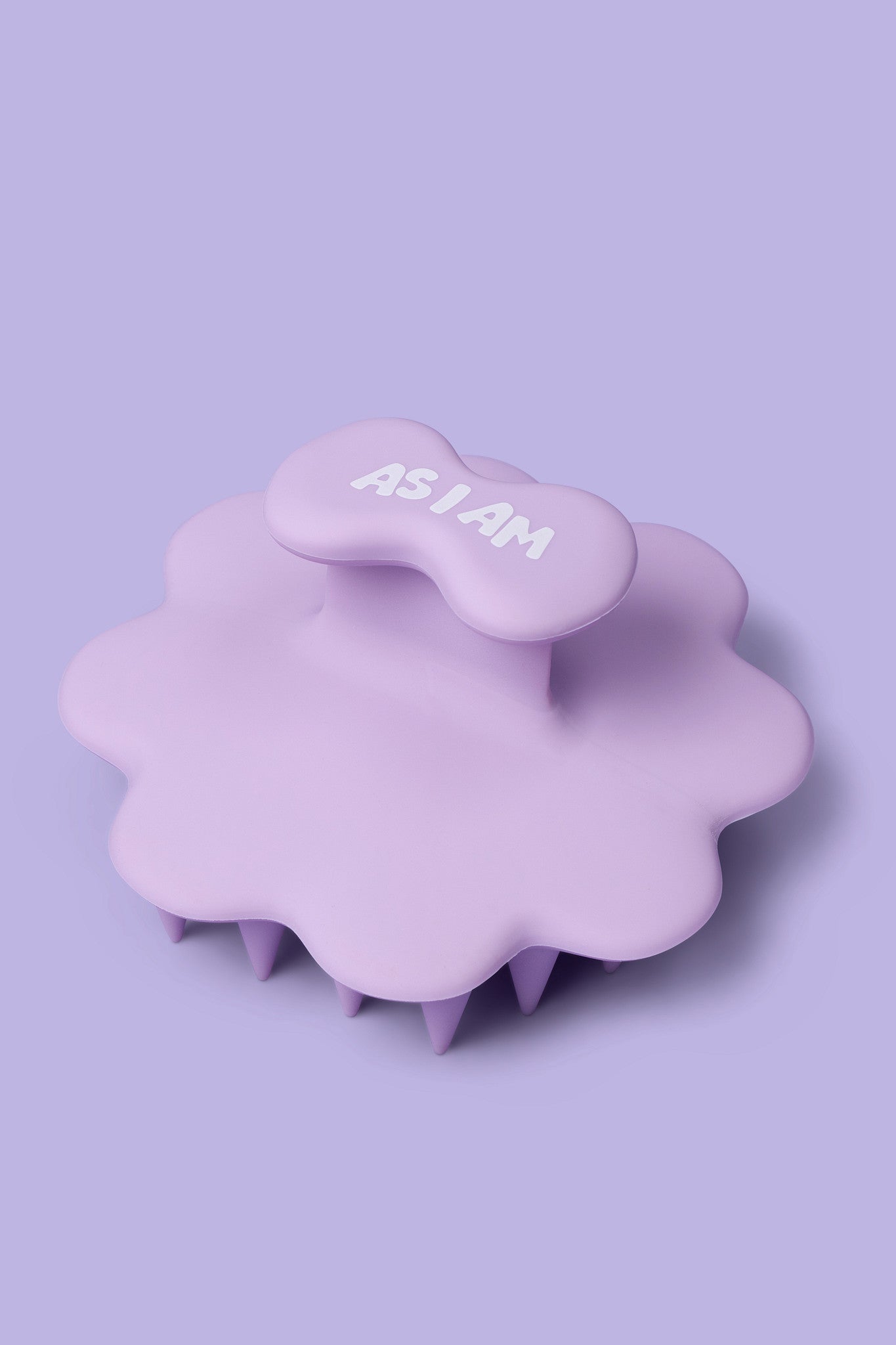 Lila Kopfhautmassagegerät mit dem Schriftzug „AS I AM” auf helllila Hintergrund