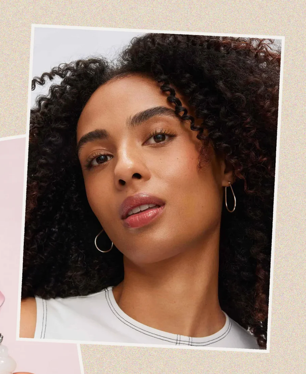 Frau mit lockigem Haar und Creolen vor beigem Hintergrund